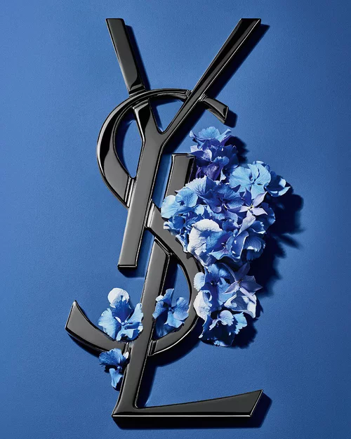 Black YSL Cassandre logo adorned with vibrant blue spring flowers, set against a serene blue background.